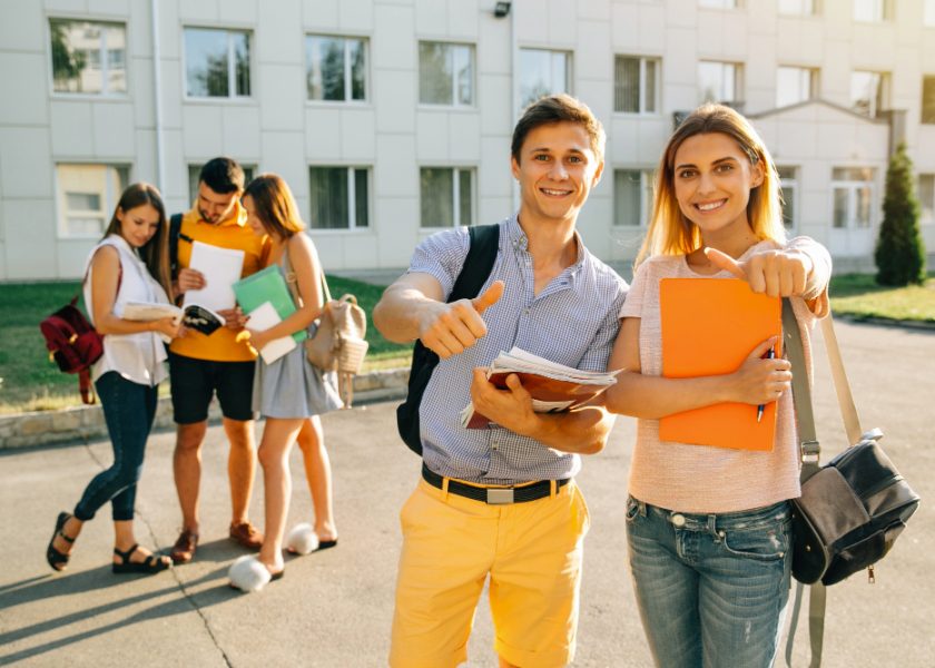 happy-two-young-students-with-note-books-backpacks-smiling-showing-thumb-up